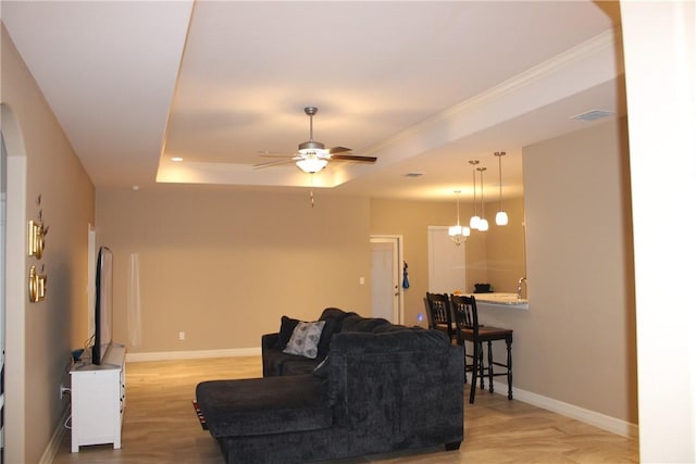 living room with ceiling fan with notable chandelier, a raised ceiling, and light wood-type flooring