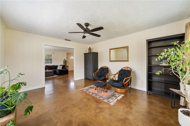 living area featuring concrete flooring, ceiling fan, visible vents, and baseboards