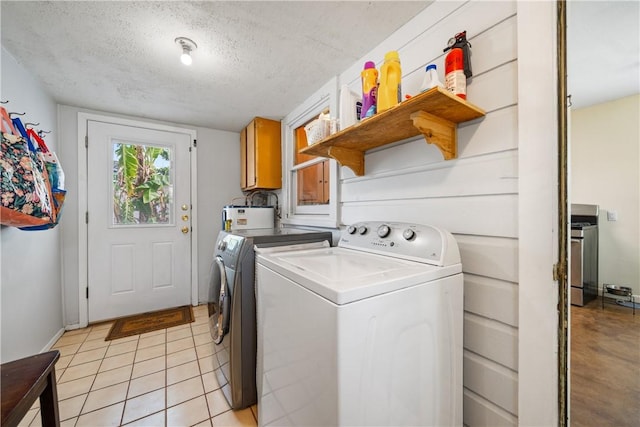 laundry room featuring a textured ceiling, washing machine and dryer, cabinet space, light tile patterned floors, and water heater