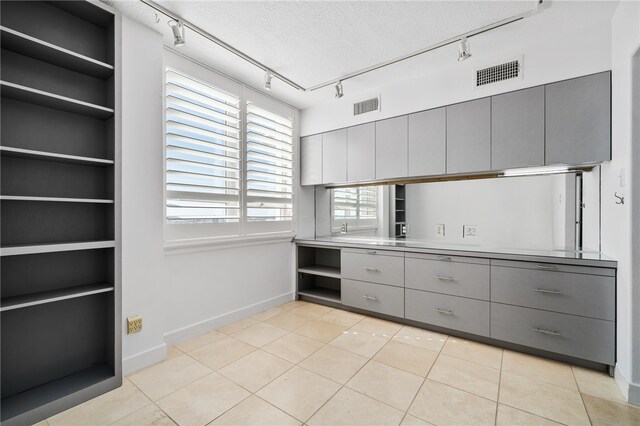 kitchen featuring track lighting, a textured ceiling, gray cabinetry, and light tile patterned flooring