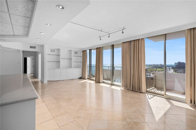 unfurnished living room with expansive windows, rail lighting, light tile patterned floors, and a water view