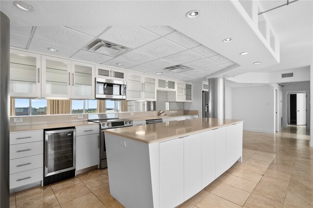 kitchen featuring white cabinetry, appliances with stainless steel finishes, light tile patterned floors, beverage cooler, and a kitchen island