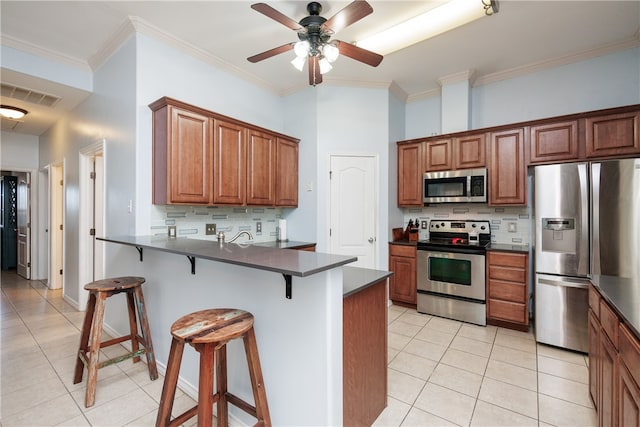 kitchen featuring kitchen peninsula, tasteful backsplash, a kitchen breakfast bar, crown molding, and appliances with stainless steel finishes