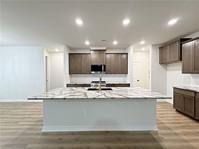 9505 Spanish Oak Dr, Corpus Christi, TX 78410 - kitchen with appliances with stainless steel finishes, decorative backsplash, an island with sink, light stone counters, and light wood-style floors
