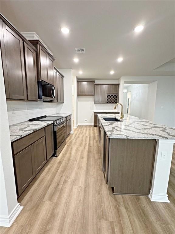 9505 Spanish Oak Dr, Corpus Christi, TX 78410 - kitchen with a sink, stainless steel appliances, light wood-style floors, an island with sink, and tasteful backsplash