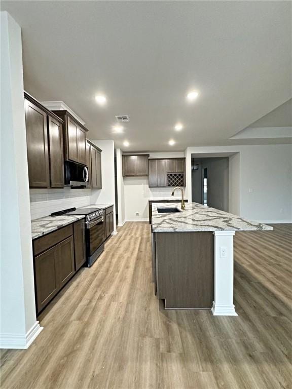 kitchen featuring light wood-type flooring, light stone counters, stainless steel appliances, a kitchen island with sink, and sink