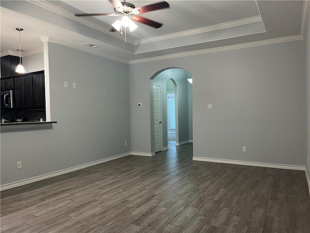 empty room with dark wood-style floors, a tray ceiling, arched walkways, and visible vents