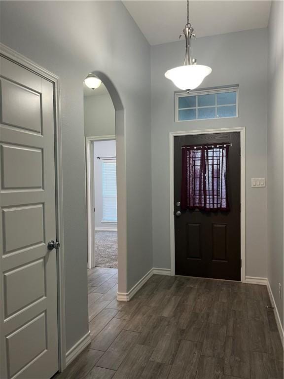 foyer entrance featuring baseboards, arched walkways, and dark wood-type flooring