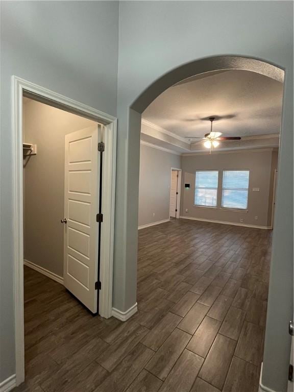 hallway featuring arched walkways, a tray ceiling, dark wood finished floors, and baseboards