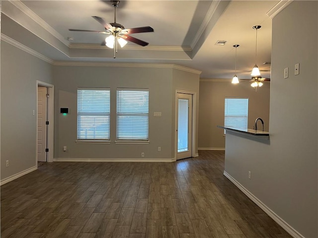 unfurnished living room featuring plenty of natural light, a raised ceiling, dark wood finished floors, and ceiling fan