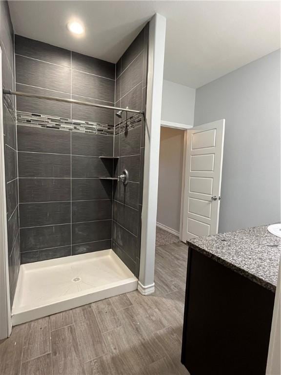 full bathroom with tiled shower, wood finished floors, vanity, and baseboards