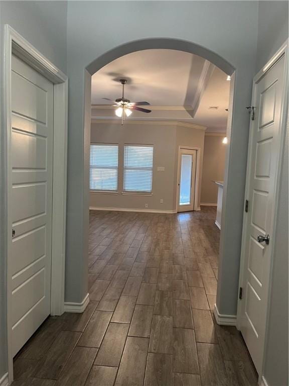 hallway featuring arched walkways, a tray ceiling, crown molding, wood tiled floor, and baseboards