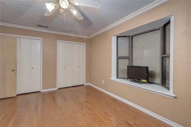 unfurnished bedroom featuring a textured ceiling, multiple closets, ceiling fan, light hardwood / wood-style floors, and ornamental molding