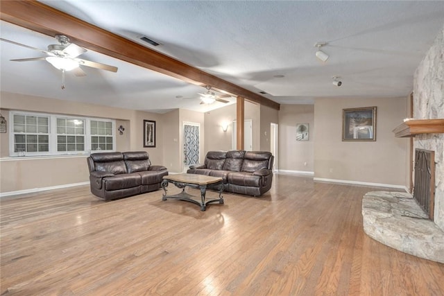 living room featuring a textured ceiling, light hardwood / wood-style floors, vaulted ceiling with beams, and a fireplace