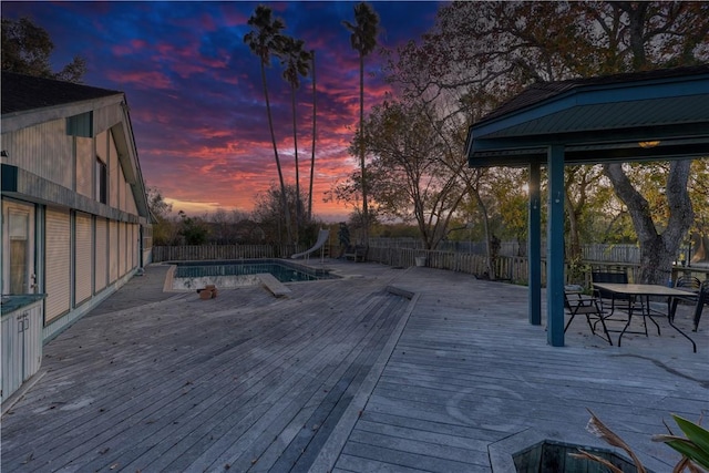 deck at dusk with a fenced in pool