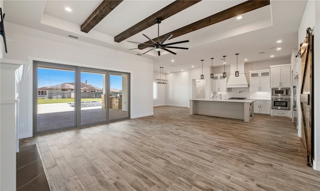 unfurnished living room featuring a barn door, beamed ceiling, light wood-style floors, and visible vents