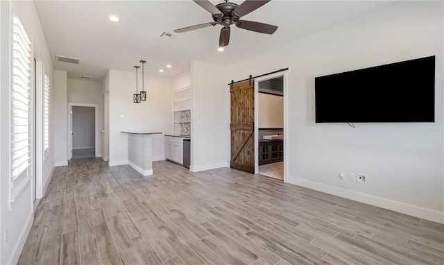 unfurnished living room featuring a barn door, recessed lighting, visible vents, and light wood finished floors