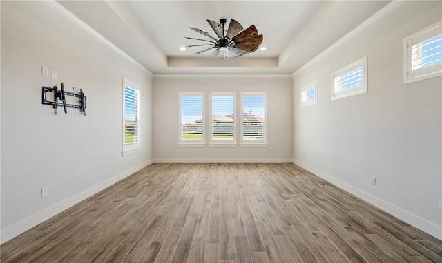 empty room with a healthy amount of sunlight, a tray ceiling, and wood finished floors