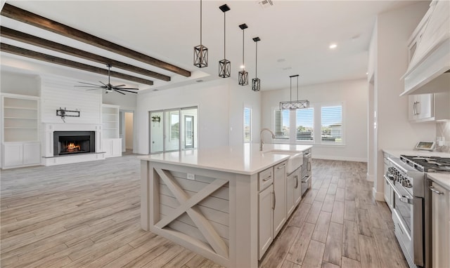 kitchen with light wood-style flooring, a ceiling fan, under cabinet range hood, a sink, and range with two ovens