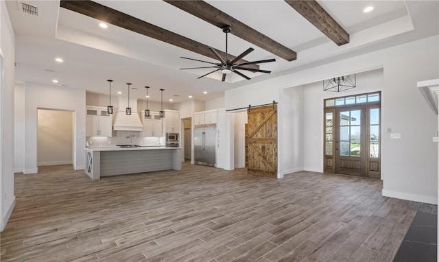 interior space featuring visible vents, baseboards, light wood-style flooring, a barn door, and beamed ceiling