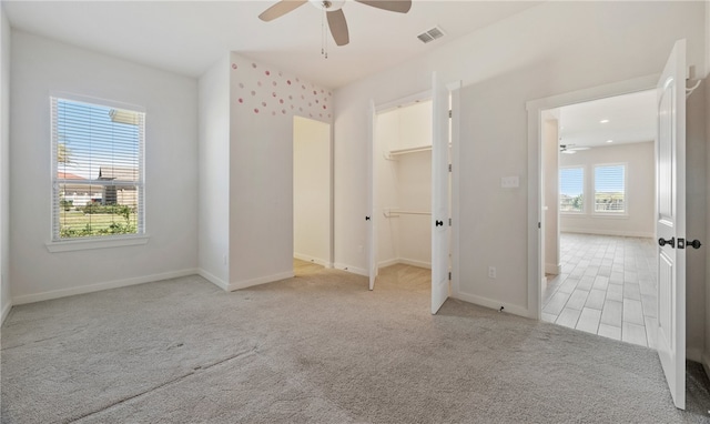 unfurnished bedroom featuring baseboards, visible vents, ceiling fan, a spacious closet, and light carpet