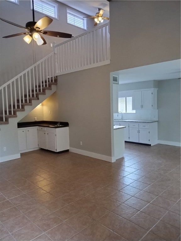 unfurnished living room featuring a high ceiling, ceiling fan, sink, and light tile patterned flooring