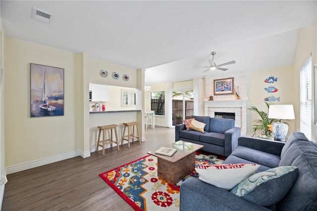 living room featuring a stone fireplace, wood-type flooring, vaulted ceiling, and ceiling fan