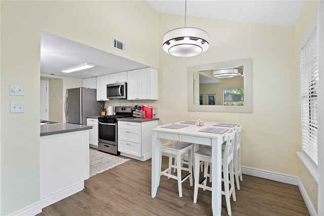 kitchen featuring white cabinets, a kitchen breakfast bar, appliances with stainless steel finishes, and dark wood-type flooring