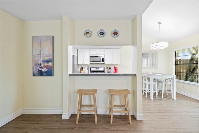 kitchen with white cabinetry, hanging light fixtures, hardwood / wood-style flooring, and stainless steel appliances