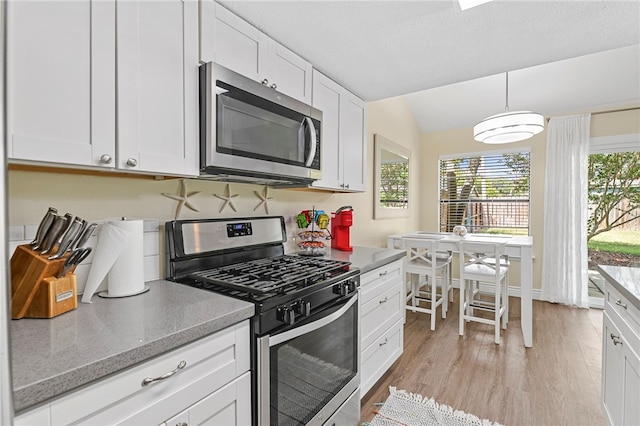 kitchen featuring stainless steel appliances, light hardwood / wood-style floors, light stone counters, vaulted ceiling, and white cabinets