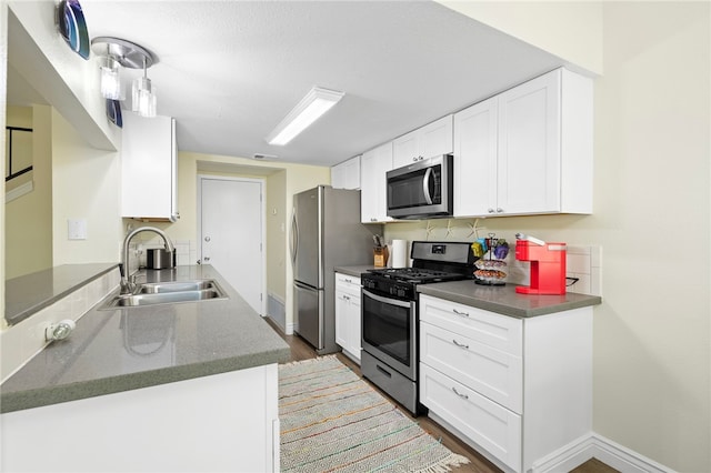 kitchen featuring dark wood-type flooring, white cabinets, kitchen peninsula, sink, and appliances with stainless steel finishes