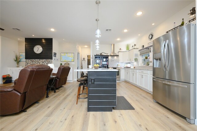 kitchen with light hardwood / wood-style floors, white cabinetry, a center island with sink, appliances with stainless steel finishes, and pendant lighting