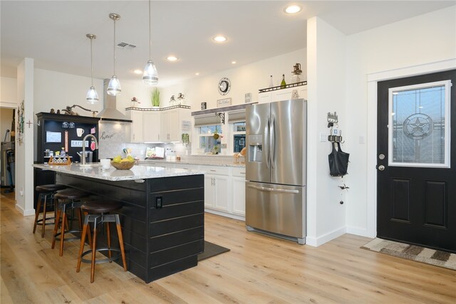 kitchen with light stone counters, stainless steel refrigerator with ice dispenser, decorative light fixtures, light hardwood / wood-style flooring, and white cabinets