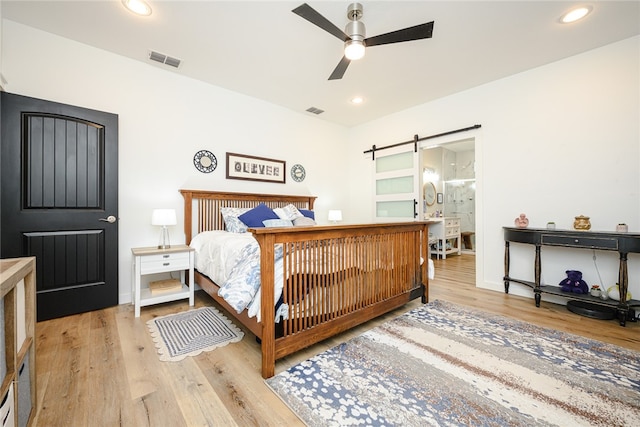 bedroom with a barn door, ceiling fan, and light hardwood / wood-style flooring