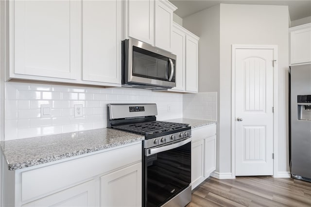 kitchen featuring decorative backsplash, appliances with stainless steel finishes, light wood-type flooring, light stone counters, and white cabinetry