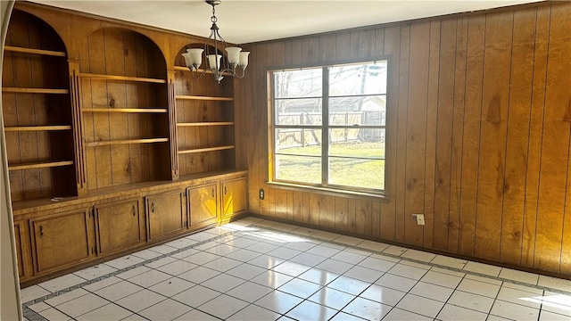 empty room with built in shelves, a chandelier, and wood walls