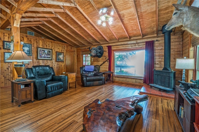 living room featuring lofted ceiling with beams, wood-type flooring, a wood stove, wooden walls, and wood ceiling