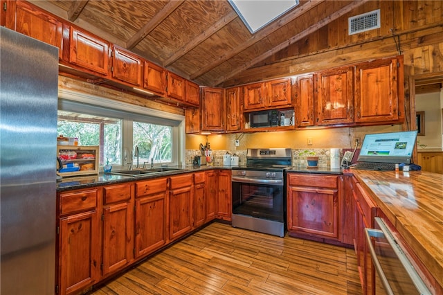 kitchen with stainless steel appliances, wooden walls, sink, lofted ceiling with skylight, and light wood-type flooring