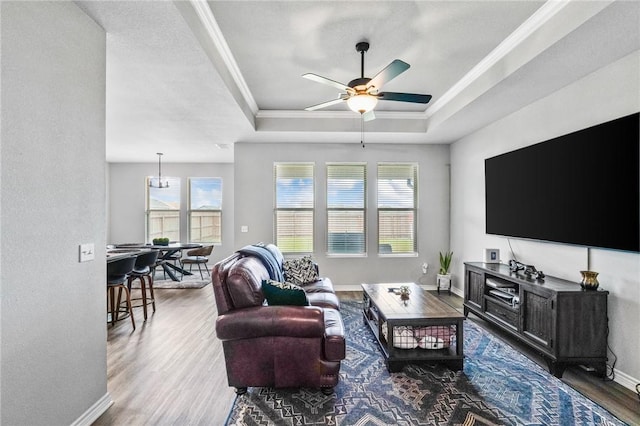 living room featuring a ceiling fan, wood finished floors, a raised ceiling, baseboards, and ornamental molding