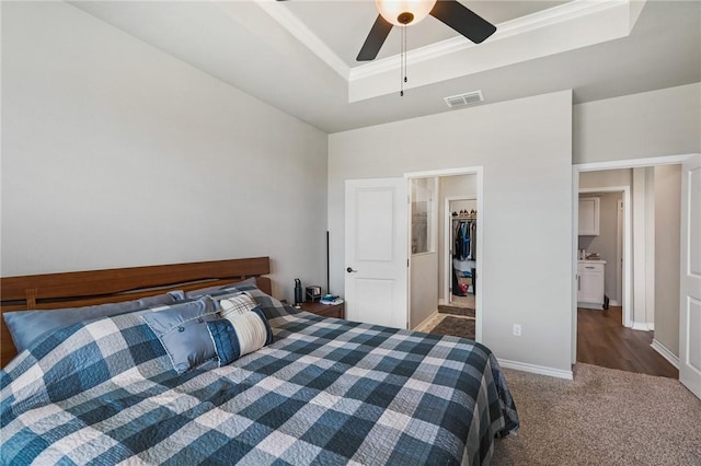 bedroom featuring a walk in closet, visible vents, carpet floors, ornamental molding, and a tray ceiling