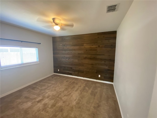 empty room featuring dark colored carpet, ceiling fan, and wood walls