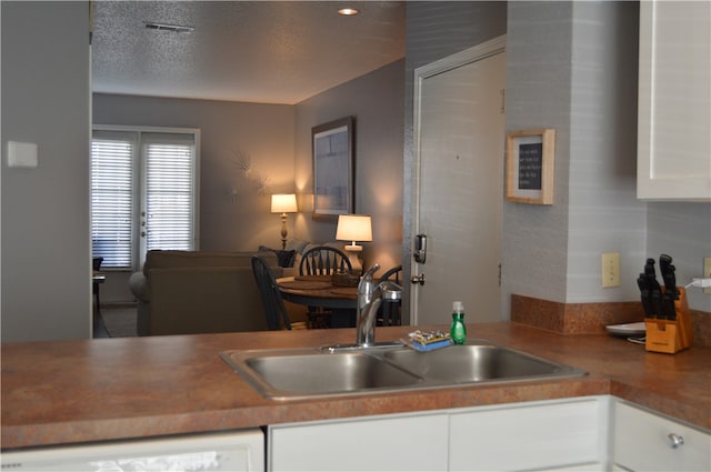 kitchen with a textured ceiling, dishwasher, sink, and white cabinets