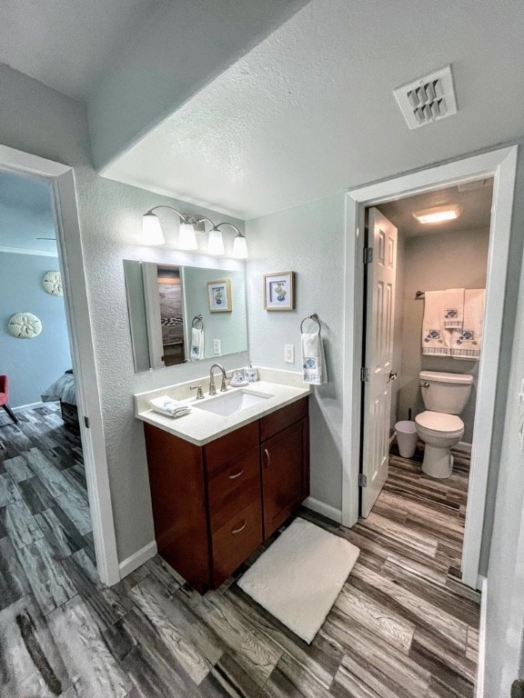 ensuite bathroom featuring wood finished floors, toilet, vanity, a textured ceiling, and baseboards