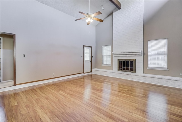 unfurnished living room featuring light hardwood / wood-style floors, a textured ceiling, high vaulted ceiling, ceiling fan, and a fireplace