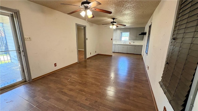 unfurnished living room featuring dark wood-style floors, ceiling fan, a textured ceiling, and baseboards