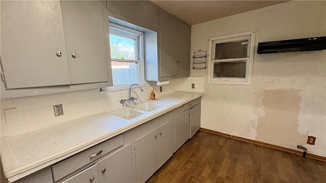 kitchen featuring a sink, dark wood finished floors, baseboards, light countertops, and gray cabinets