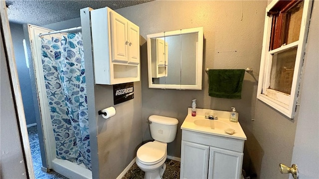 bathroom with a stall shower, vanity, toilet, a textured ceiling, and baseboards