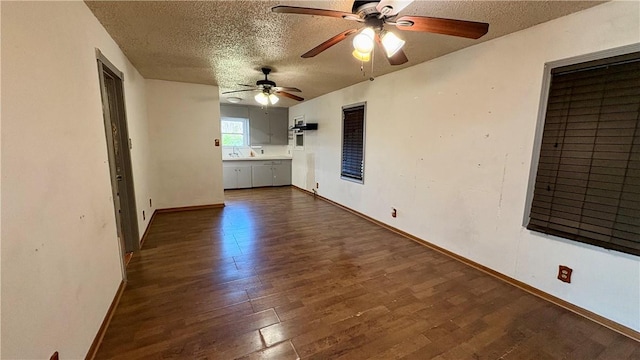 empty room featuring a textured ceiling, dark wood-type flooring, ceiling fan, and baseboards