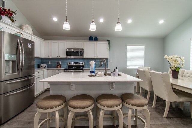 kitchen with pendant lighting, appliances with stainless steel finishes, a center island with sink, and white cabinets