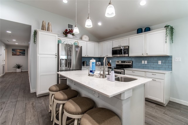 kitchen featuring stainless steel appliances, white cabinetry, hanging light fixtures, a kitchen island with sink, and vaulted ceiling